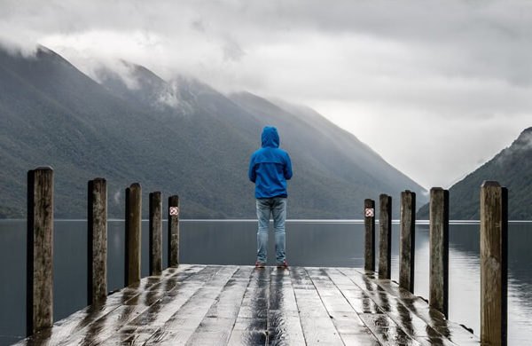 Person auf Steg vor wolkenverhangenen Bergen